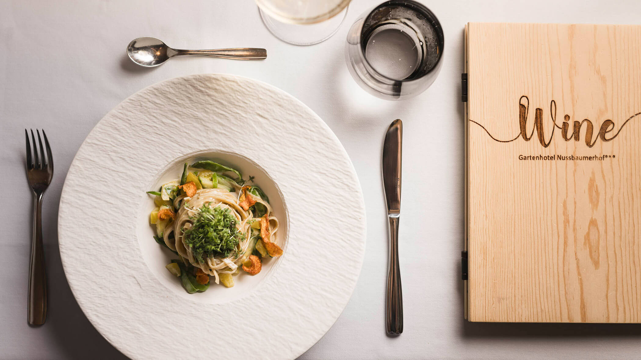 Nudelgericht und die Weinkarte auf dem gedeckten Tisch